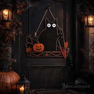 May include: A black cat wall hanging decoration featuring large white eyes, a small orange jack-o'-lantern, and a large knife with red blood-like markings. The piece is suspended by a rope and includes decorative scrollwork along the bottom edge.