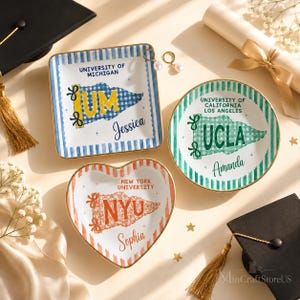 May include: Three ceramic trinket dishes with gold-toned rims. One square dish features a blue University of Michigan pennant and the name Jessica. One round dish shows a green UCLA pennant and the name Amanda. One heart-shaped dish displays an orange NYU pennant and the name Sophia.