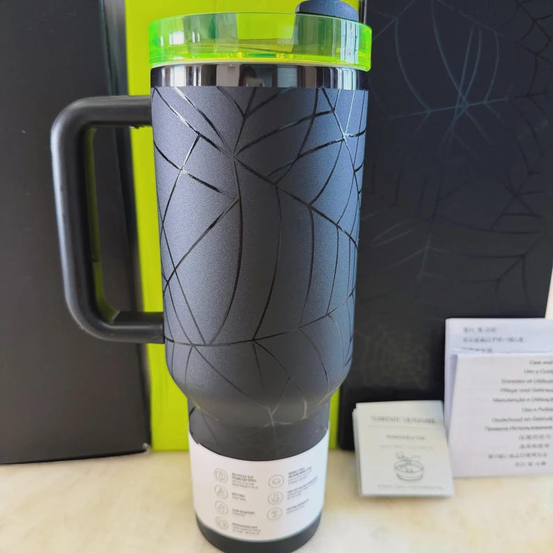 May include: A black insulated travel mug with a geometric pattern, a black handle, and a neon green lid. The mug has a capacity of approximately 887 ml. Designed to keep drinks cold or hot for hours.