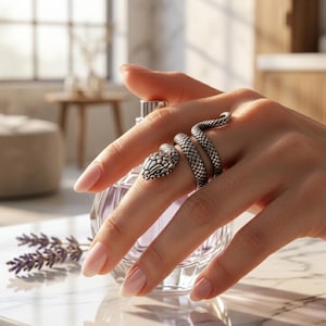 Puede incluir: Un anillo de metal plateado con forma de serpiente enroscada, con escamas texturizadas y un diseño de cabeza detallado. El anillo se envuelve alrededor del dedo, presentando un acabado metálico que resalta el intrincado patrón del cuerpo y la cabeza.