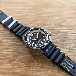Peut inclure: Une montre-bracelet noire et argent&eacute;e avec un bracelet en caoutchouc noir. Le cadran de la montre est noir avec des marquages et des aiguilles blancs. La montre est sur une surface en bois.