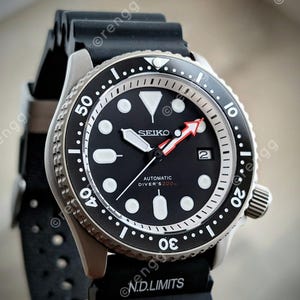 Peut inclure: Gros plan d'une montre de plong&eacute;e automatique Seiko noire avec un cadran noir, des marqueurs blancs et une aiguille des secondes &agrave; pointe rouge. La montre a une lunette en acier inoxydable et un bracelet en caoutchouc noir. Le cadran affiche le texte "SEIKO AUTOMATIC DIVER'S 200m".
