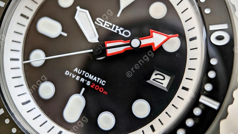 Peut inclure: Gros plan d'une montre de plong&eacute;e automatique Seiko noire. Le cadran de la montre comporte des index blancs, une fen&ecirc;tre de date et une aiguille des secondes en forme de fl&egrave;che rouge et blanche. La montre est &eacute;tanche &agrave; 200 m.