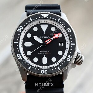 Peut inclure: Une montre de plong&eacute;e automatique Seiko noire avec un cadran noir, des marqueurs blancs et une aiguille des secondes &agrave; pointe rouge. La montre a une lunette en acier inoxydable et un bracelet en caoutchouc noir. Le texte "SEIKO" et "AUTOMATIC DIVER'S 200m" est visible.