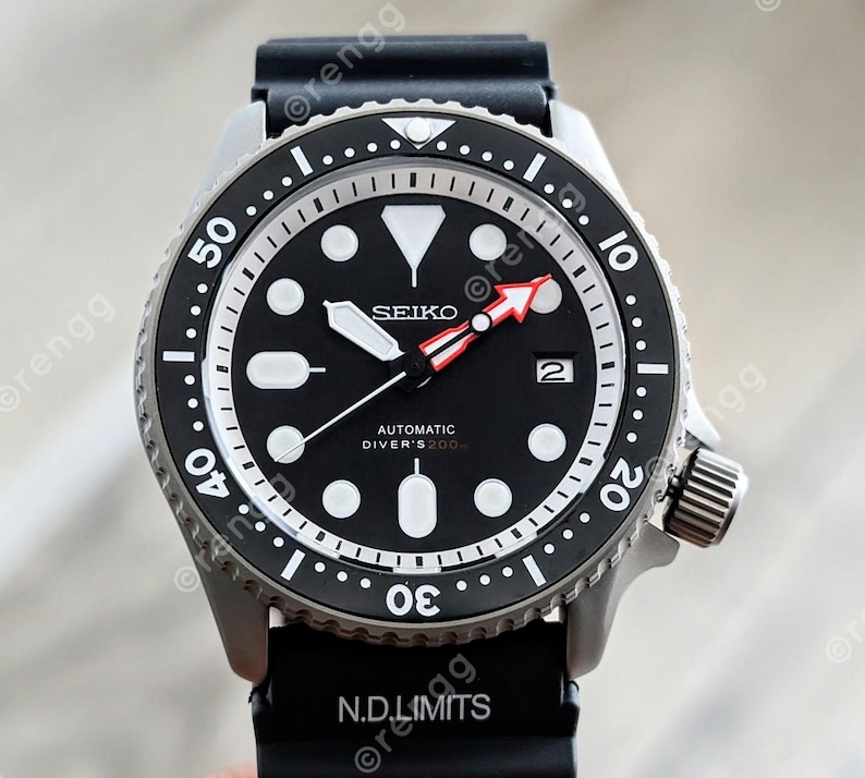 Peut inclure: Une montre de plong&eacute;e automatique Seiko noire avec un cadran noir, des marqueurs blancs et une aiguille des secondes &agrave; pointe rouge. La montre a une lunette en acier inoxydable et un bracelet en caoutchouc noir. Le texte "SEIKO" et "AUTOMATIC DIVER'S 200m" est visible.