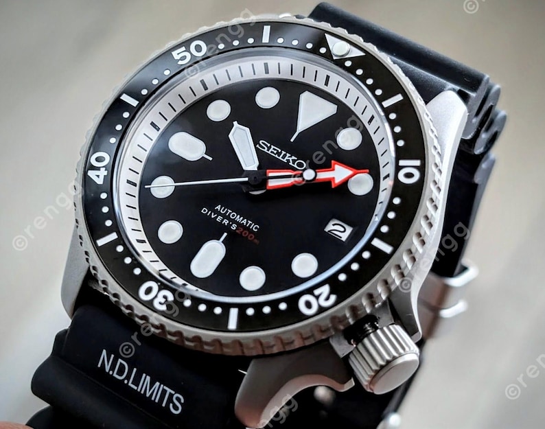 Peut inclure: Une montre de plong&eacute;e automatique Seiko noire avec une lunette noire et un bracelet en caoutchouc noir. Le cadran est noir avec des marqueurs et des aiguilles blancs, et une aiguille des secondes rouge. R&eacute;sistant &agrave; l'eau jusqu'&agrave; 200m.