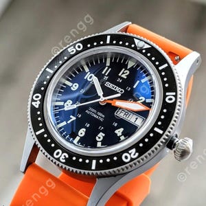 May include: A close-up of a Seiko watch with a black and silver bezel and a blue face. The watch has an orange band and the day is Friday. The watch face displays the time and the word "SEIKO".