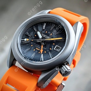 May include: A Seiko Black Carbon GMT automatic watch with a black dial and orange accents. The watch has a silver-colored case and an orange rubber strap. The watch face displays the date and time.
