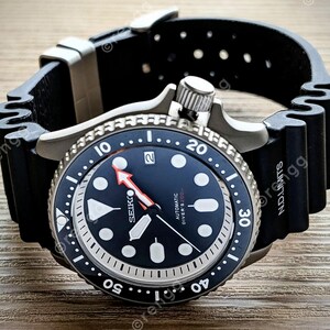 Peut inclure: Une montre de plong&eacute;e automatique Seiko noire et argent&eacute;e avec un bracelet en caoutchouc noir. Le cadran est bleu fonc&eacute; avec des marqueurs blancs et une aiguille des secondes rouge. La lunette a des marquages blancs et le bracelet porte l'inscription "N.D. Limits".