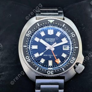 May include: A stainless steel Seiko automatic watch with a blue dial and a black rotating bezel. The watch features luminous hands and markers, a date window, and is water-resistant to 150 meters.