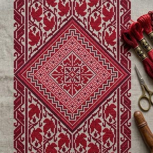 May include: A detailed cross-stitch pattern in shades of red on a neutral linen background. The design features a central diamond shape with floral and geometric motifs. Red embroidery floss, scissors, and a wooden tool are visible.