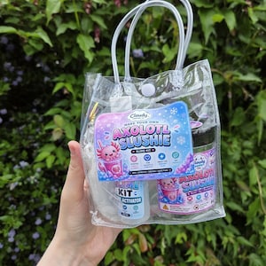 May include: A clear plastic tote bag containing a Cloudy Company Make Your Own Axolotl Slushie slime kit. The kit includes a bottle of slime activator and a jar labelled Axolotl Slushie, both featuring cartoon axolotl graphics and blue and pink text.