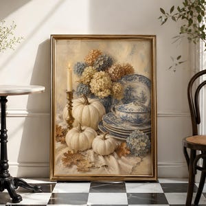 May include: A framed painting depicting a still life scene with three white pumpkins, a tall brass candlestick with a lit candle, a stack of blue and white patterned ceramic plates, and clusters of dried hydrangea flowers on a textured cloth.