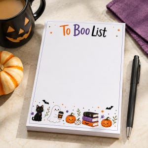 May include: A rectangular notepad with the text To Boo List printed in orange and purple at the top. The bottom border features colourful illustrations of a black cat, a ghost holding a coffee cup, pumpkins, stacked books, and bats.