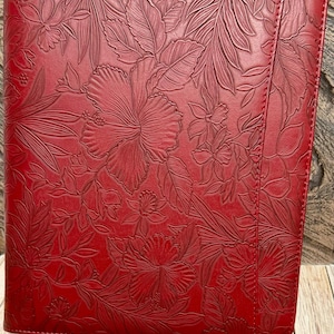 May include: A rectangular red portfolio case featuring an embossed floral pattern across the entire front surface. The design includes detailed depictions of hibiscus flowers and various tropical leaves, with a vertical stitched seam on the right side.
