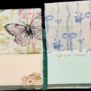 May include: Four square paper notepads with upright decorative covers. The first cover has a pink gingham and bow pattern with the text MAKE IT HAPPEN. The second features a black butterfly illustration. The third has blue bows and the text GET IT DONE. The fourth displays a pink bow pattern.