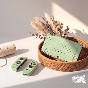 Peut inclure: Un étui de tablette vert menthe et deux manettes de jeu assorties à pois noirs sont présentés dans un panier en osier. Un rouleau de ficelle et des fleurs séchées sont également dans l'image. Le texte "Johns Show" est dans le coin inférieur droit.