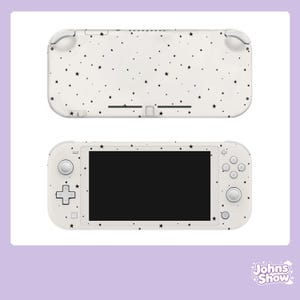 Può includere: Una console di gioco portatile con un esterno bianco e un motivo a stelle nere sparse. Il dispositivo è mostrato sia dalla prospettiva frontale che da quella posteriore, evidenziando lo schermo, il pad direzionale, i tasti e gli stick.