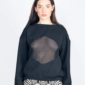 May include: A black long-sleeved sweatshirt with a hexagonal mesh panel on the front. The sweatshirt is paired with black and white patterned shorts.