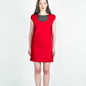 May include: A woman wearing a red sleeveless dress with a black mesh neckline and black heeled sandals.