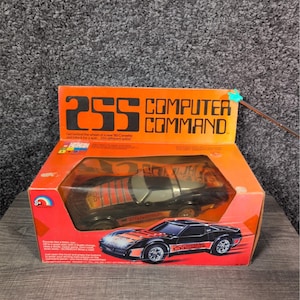 May include: A vintage toy car in its original box. The box is orange and red with the text "255 COMPUTER COMMAND". The car is black with orange and red stripes. The box also features an image of the car.