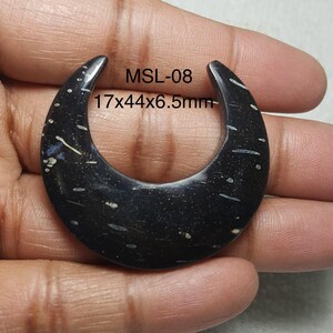 May include: A black, crescent-shaped pendant with white and light blue speckles and streaks. The text "MSL-08" and measurements of 0.67 x 1.73 x 0.26 inches are visible. The pendant is held in a hand.
