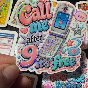 Op de afbeelding: Een holografische sticker met een zilveren klaptelefoon waarop het scherm 09:00 PM en een hartpictogram toont. De tekst Call me after 9 it's free staat in roze en blauwe bubbelletters, versierd met kleine sterretjes, hartjes en tekstballonnen.