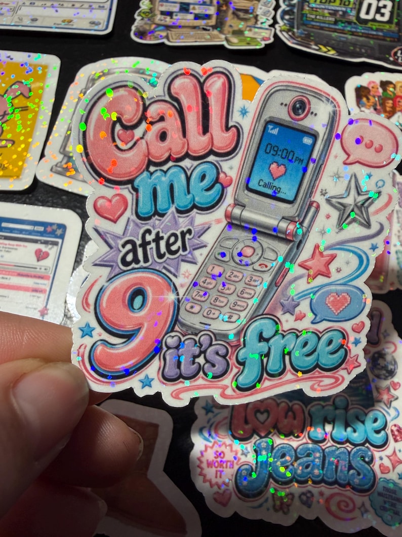 Op de afbeelding: Een holografische sticker met een zilveren klaptelefoon waarop het scherm 09:00 PM en een hartpictogram toont. De tekst Call me after 9 it's free staat in roze en blauwe bubbelletters, versierd met kleine sterretjes, hartjes en tekstballonnen.
