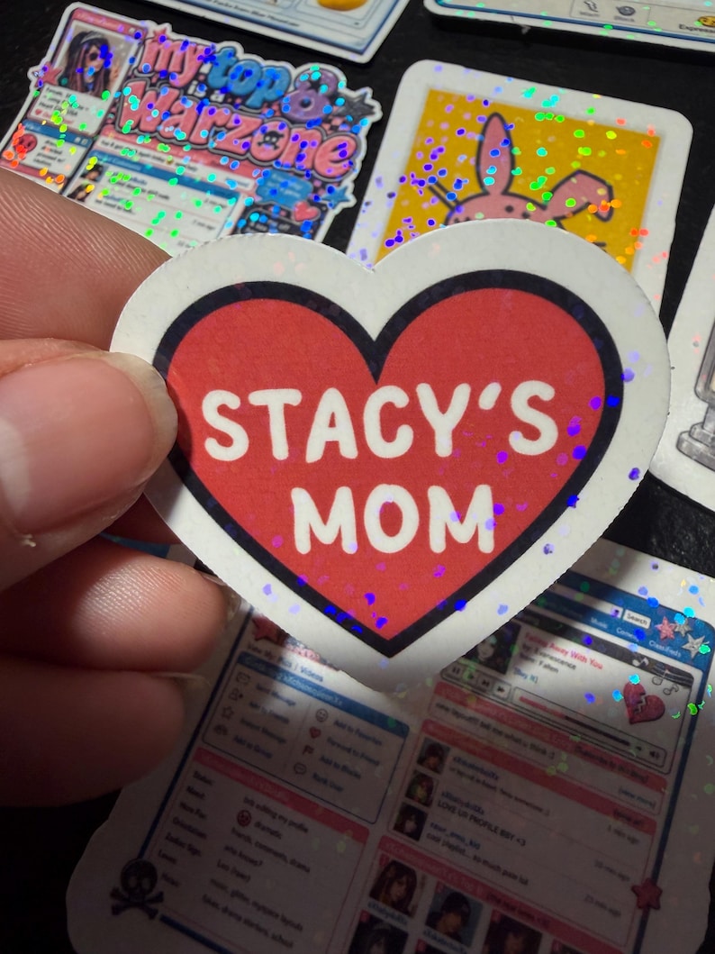 Op de afbeelding: Een hartvormige sticker met een rood midden en een dikke zwarte rand. De tekst STACY'S MOM is in dikke witte hoofdletters in het midden van het hart gedrukt. De sticker heeft een subtiele holografische afwerking die licht reflecteert.