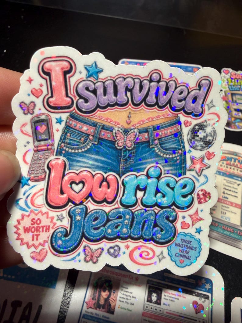 Op de afbeelding: Een holografische sticker met een blote buik in een blauwe spijkerbroek met lage taille, een vlinderriemgesp en een navelpiercing. Tekst: I survived low rise jeans, so worth it, en those waistbands were criminal. Inclusief een klaptelefoon en discobal.