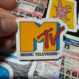 Op de afbeelding: Een gestanste sticker met het MTV-logo, bestaande uit een grote gele blokletter M en een rode, in script geschreven TV, omlijnd in blauw. Onder het logo staat de tekst MUSIC TELEVISION in zwarte hoofdletters op een witte achtergrond.