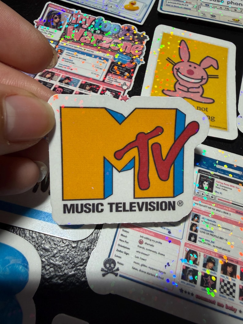 Op de afbeelding: Een gestanste sticker met het MTV-logo, bestaande uit een grote gele blokletter M en een rode, in script geschreven TV, omlijnd in blauw. Onder het logo staat de tekst MUSIC TELEVISION in zwarte hoofdletters op een witte achtergrond.