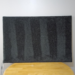 May include: A rectangular, black, textured rug with vertical stripes. The rug is placed on a light-colored wooden table. The rug has a cord attached to it.