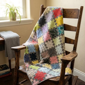 May include: A handmade patchwork quilt draped over a wooden rocking chair. The quilt features a variety of colorful fabric squares in shades of red, yellow, blue, and green. The chair is made of dark wood and has a classic design.