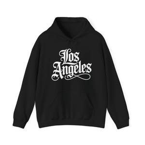 May include: A black long-sleeve hooded sweatshirt featuring the text Los Angeles printed in a white gothic-style font across the chest. The garment includes a front kangaroo pocket, a drawstring hood, and ribbed cuffs at the sleeves and hem.