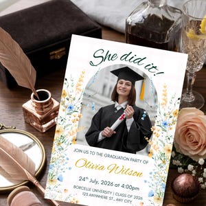 Peut inclure: Une carte d'invitation pour une fête de remise de diplôme avec le texte She did it! et la photo d'une personne diplômée en toge et mortier noirs tenant un diplôme. La carte est ornée d'illustrations florales jaunes et bleues avec le nom Olivia Wilson.