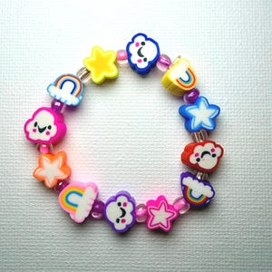 May include: A colorful bracelet featuring various charms, including stars, clouds, and rainbows. The charms are in shades of yellow, pink, blue, and orange, strung together with pink beads. A playful accessory.