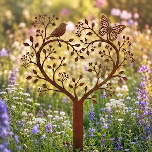 May include: A rust-colored metal garden stake featuring a heart-shaped tree silhouette. The design includes a small bird perched on the left branch and a butterfly resting on the right branch, with intricate leaf and twig details throughout the structure.