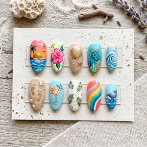 May include: A set of ten press-on nails with various beach-themed designs. Each nail features unique artwork, including sunsets, hibiscus flowers, seashells, turtles, waves, footprints, cocktails, palm leaves, rainbows, and whales.