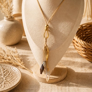 Peut inclure: Un long collier doré composé d'un cordon lisse, d'une perle centrale dorée et d'un pendentif composé d'une forme de feuille en métal doré, d'une perle géométrique marron foncé, d'une perle grise et d'un anneau transparent.