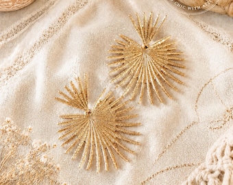 May include: A pair of gold-toned earrings featuring a sunburst design with radiating textured spikes. The earrings consist of a smaller top fan shape connected to a larger circular fan shape. A circular logo with the text BOHO BADDIE CO. BOHO CHIC WITH ATTITUDE is visible in the upper right corner.
