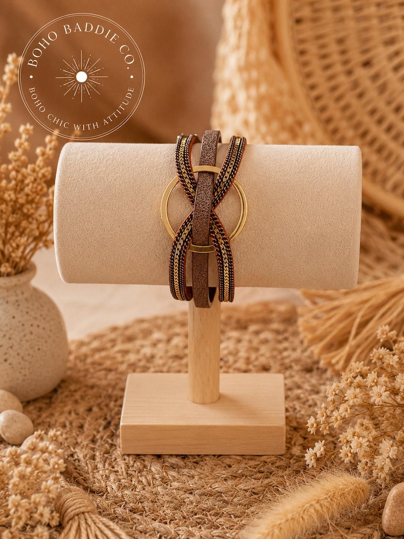 May include: A multi-strand wrap bracelet featuring a central gold-toned metal ring, a brown textured leather-like strap, and two flanking metallic chain strands in a dark bronze finish, all secured together in a layered, crisscross design.