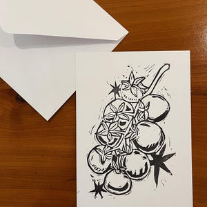 Op de afbeelding: Een witte rechthoekige wenskaart met een zwarte inktblokdrukillustratie van een tros tomaten aan de tak. Het ontwerp bevat gestileerde stervormige accenten en wordt vergezeld door een bijpassende, effen witte envelop.