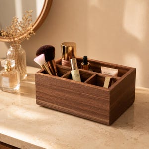 Puede incluir: Un organizador de maquillaje de madera marrón oscuro con múltiples compartimentos, que contiene brochas de maquillaje, perfume y otros productos de belleza. El organizador está sobre una superficie de color claro. Un espejo redondo es visible en el fondo.