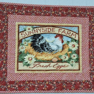 Può includere: Un arazzo da parete trapuntato rosso e bianco con un tema da fattoria. Al centro, un cartello che recita "Sunnyside Farm Fresh Eggs" con un gallo bianco e nero e un nido di uova.