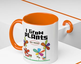 May include: A white ceramic mug with a bright orange interior and handle. The exterior features the black text "I Grow PLANTS" above a red oval containing "NOT WEEDS" and a colorful graphic of stylized flowers with multi-colored petals.