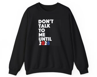 May include: A black long-sleeve sweatshirt featuring white text that reads DON'T TALK TO ME UNTIL, followed by the number 2028 in red and blue digits. The garment has a crew neckline, long sleeves with ribbed cuffs, and a ribbed hemline.