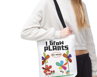 May include: A white tote bag with a black shoulder strap featuring the text I GROW PLANTS in bold black letters and NOT WEEDS in a red oval. The design includes colorful stylized flowers with petals in red, orange, yellow, blue, and purple.