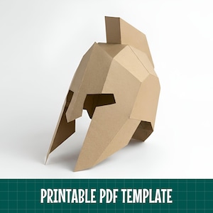Può includere: Un elmo spartano in cartone color marrone chiaro con un design geometrico low-poly, dotato di una cresta centrale e di una maschera facciale aperta. L'oggetto è presentato come modello PDF stampabile, con il testo PRINTABLE PDF TEMPLATE in basso.