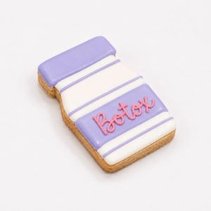 May include: A bottle-shaped sugar biscuit decorated with white and lavender icing stripes. The biscuit features the word Botox written in raised pink icing across the centre. The edges of the biscuit show the baked golden-brown texture of the dough.